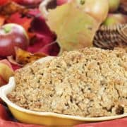 Freshly baked apple crisp with fresh apples and autumn leaves in the background.