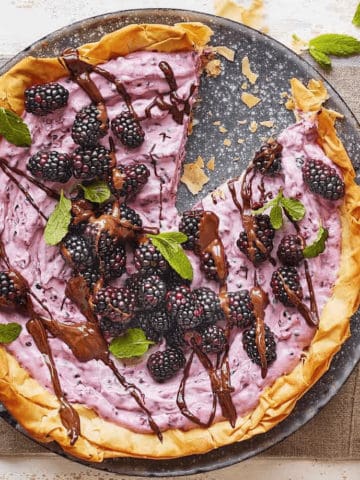 A blackberry tart on a dish with one piece of it already eaten.