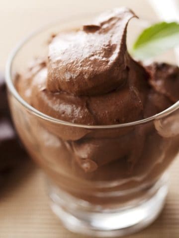 A closeup of fresh chocolate mousse in a glass with a spoon.