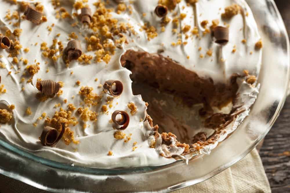 A french chocolate silk pie in a dish with one piece missing.