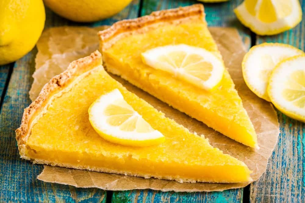 Two pieces of lemon tart with a slice of lemons on the top.