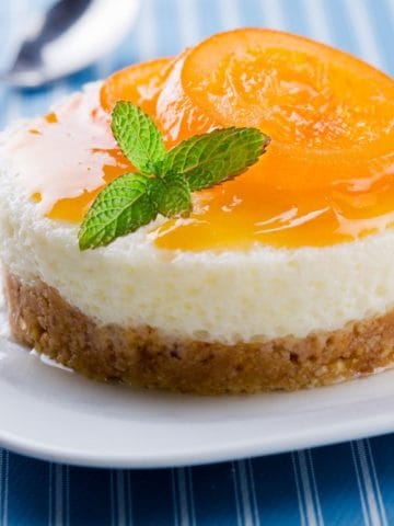A peach cheesecake bite on a white plate with a spoon next to it.