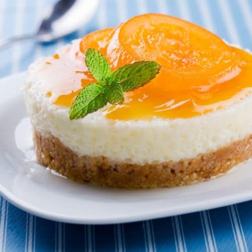 A peach cheesecake bite on a white plate with a spoon next to it.