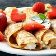 Three strawberry creamy crepes on a white plate with strawberries on top.