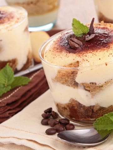 Four cups of Tiramisu on a table next to each other with spoons.