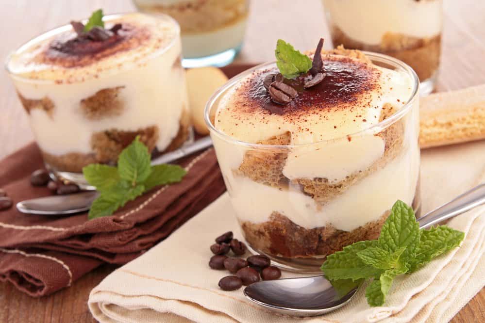 Four cups of Tiramisu on a table next to each other with spoons.