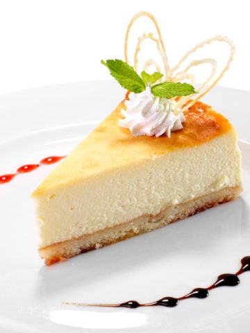 A piece of white chocolate cheesecake on a white plate with whipped cream on the top.