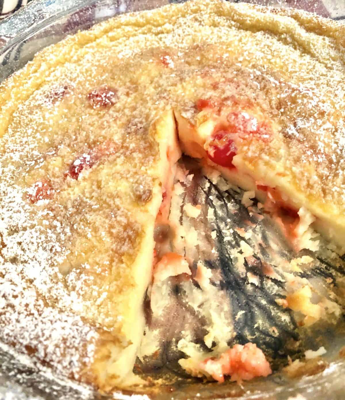 A closeup of simple French cherry clafoutis with a piece cut out of it.
