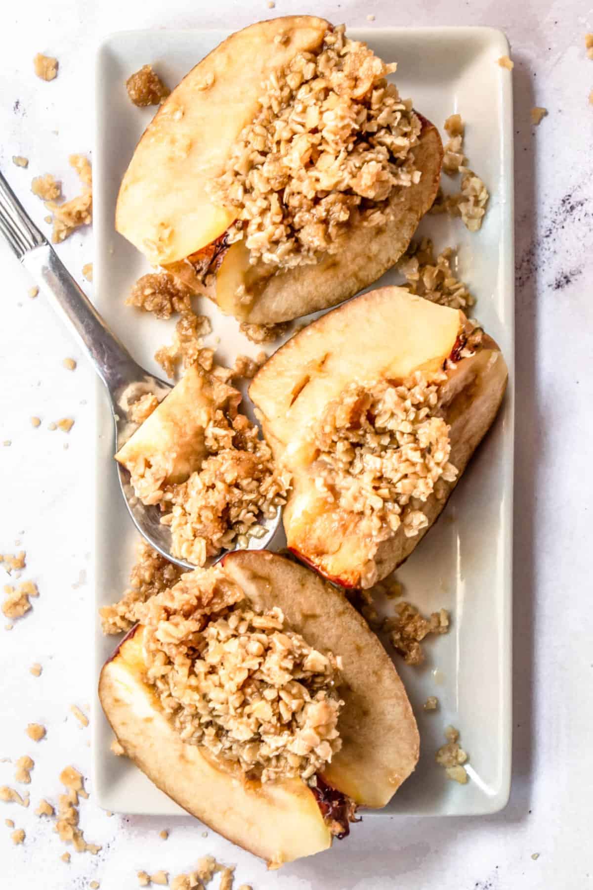 Three slices of the best oatmeal baked apples on a serving dish with a spoon.