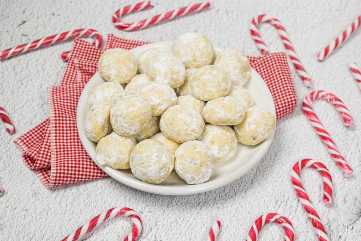 A plate of pecan cookie snowballs with candy canes.