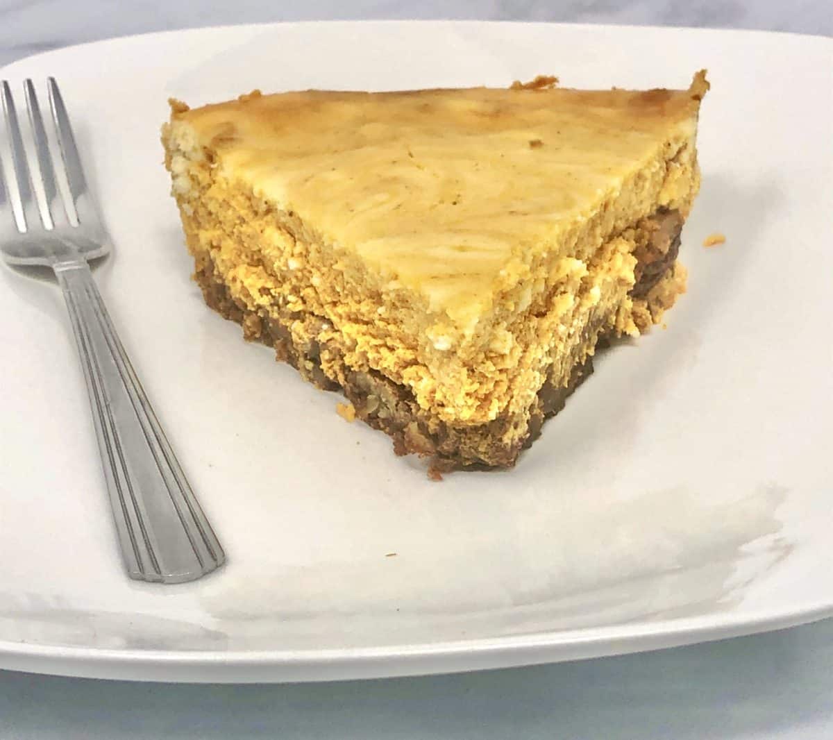 A slice of marble pumpkin cheesecake on a plate with a fork.