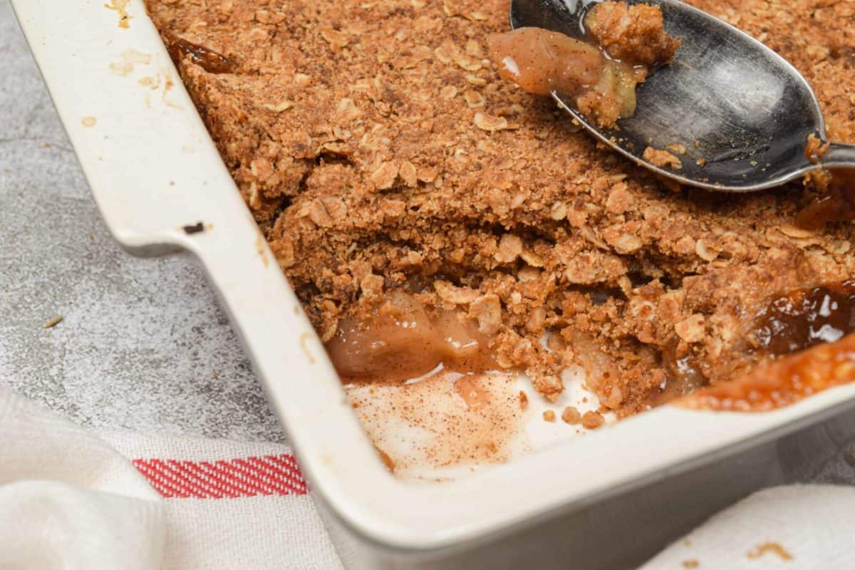 A dish of old fashioned apple crisp with a spoonful missing.