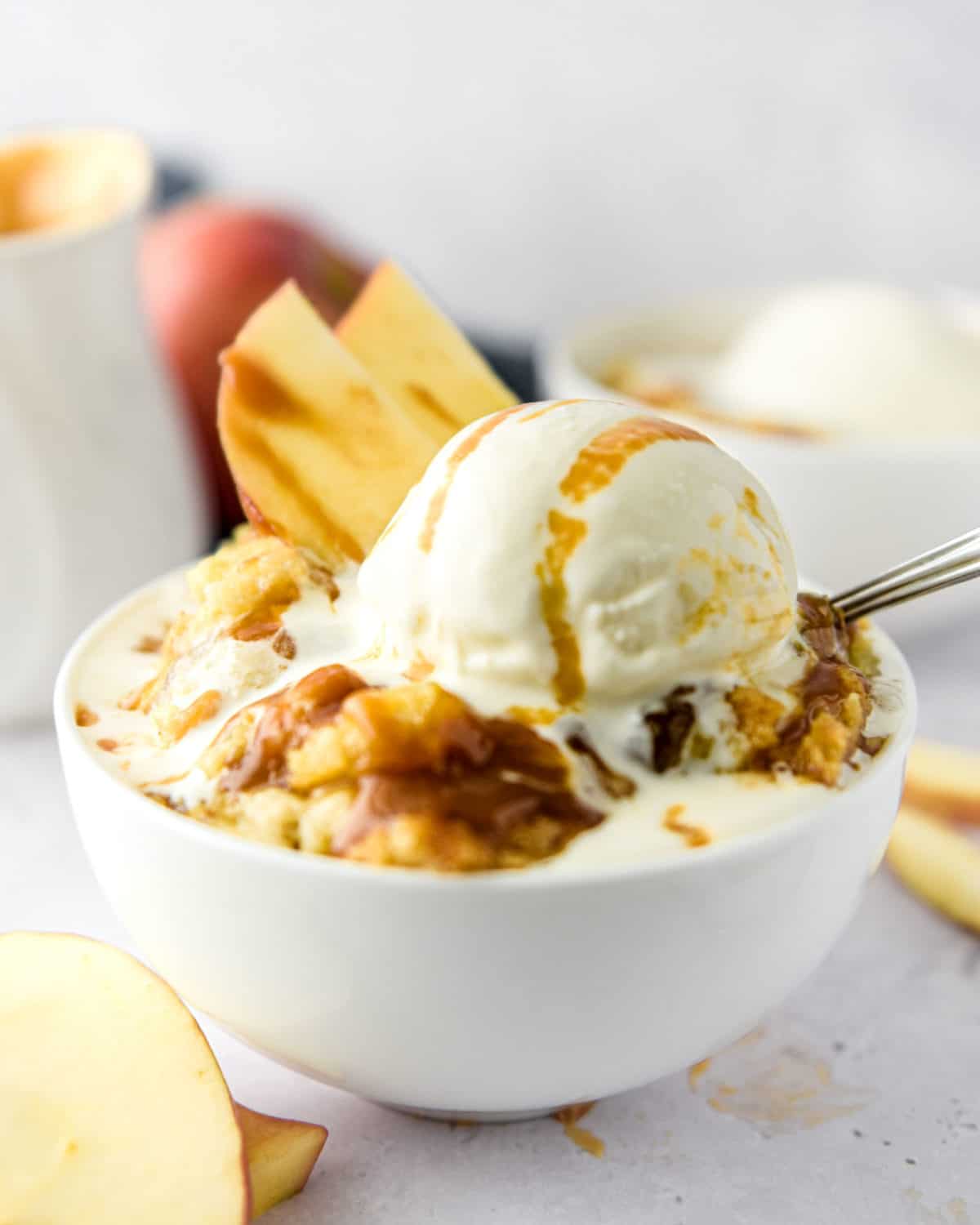 A bowl of apple dump cake with vanilla ice cream melting on it topped with caramel.