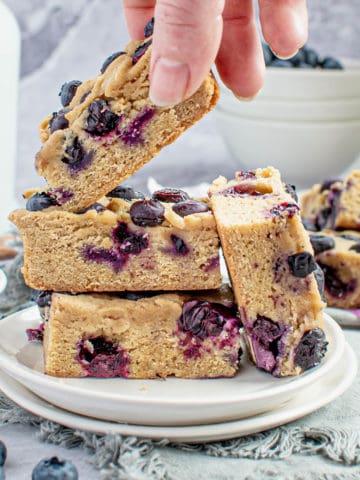 A hand placing a blueberry blondie onto a plate with others.