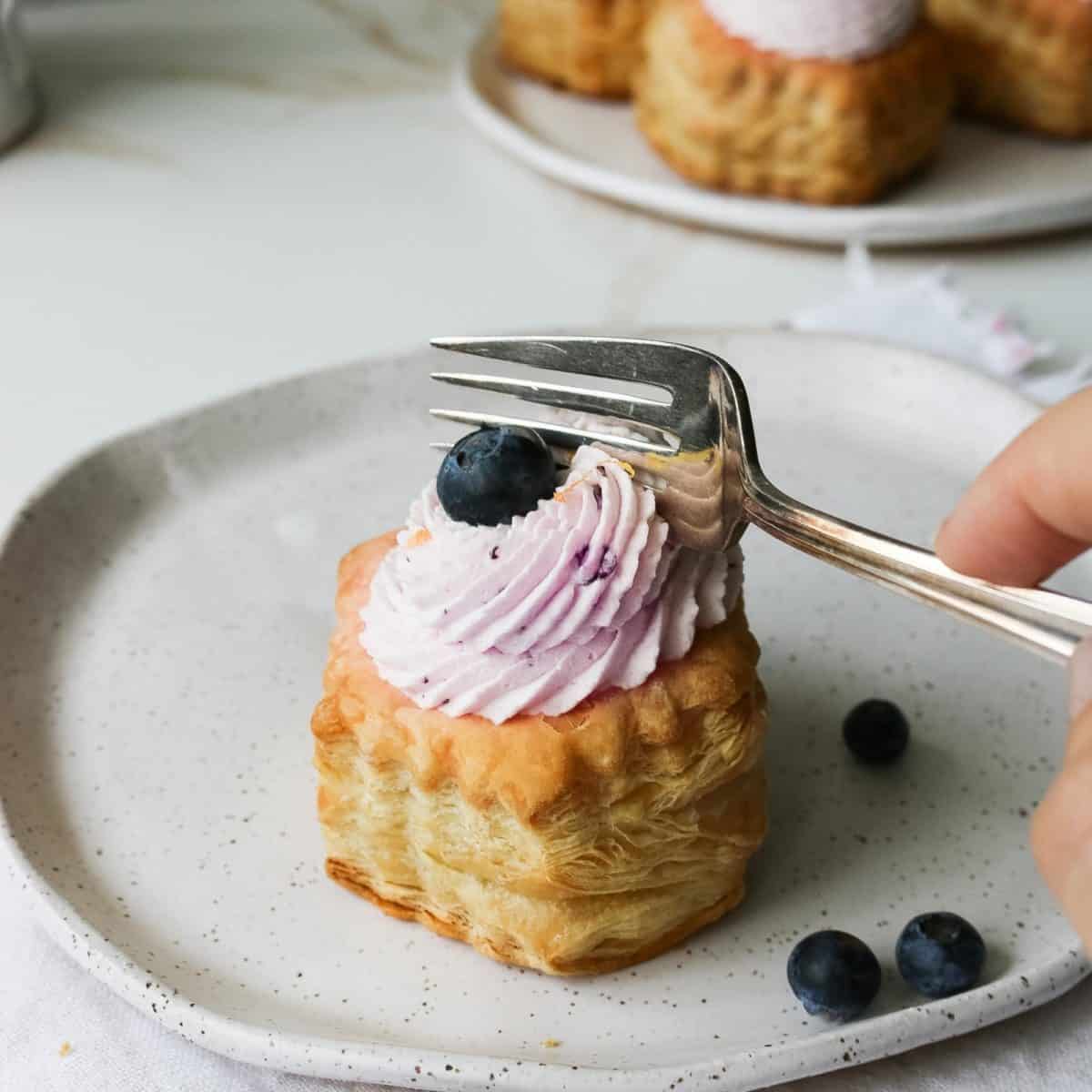 A fork cutting into a blueberry mousse puffy pastry.