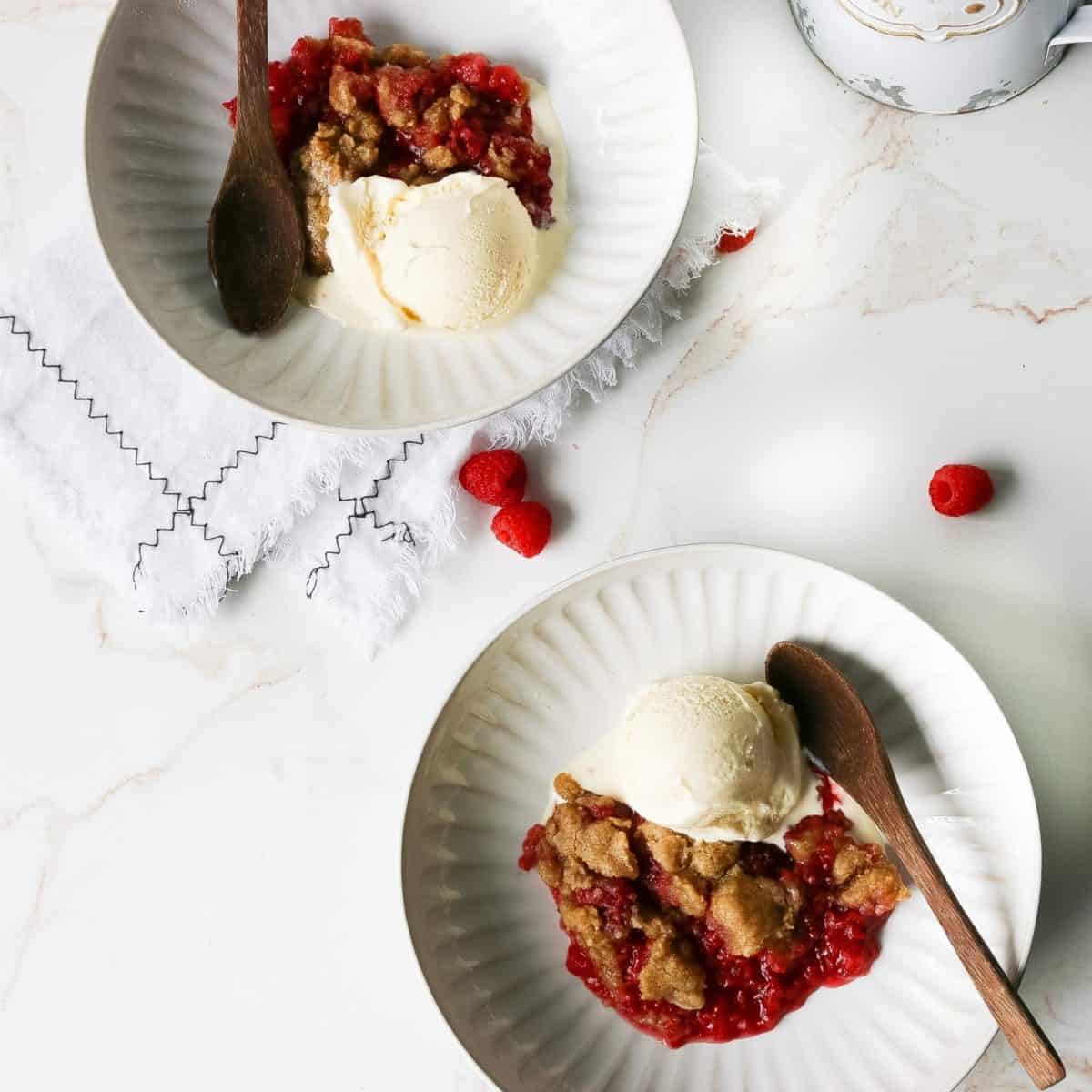 Two bowl of crisp with raspberries and topped with ice cream.