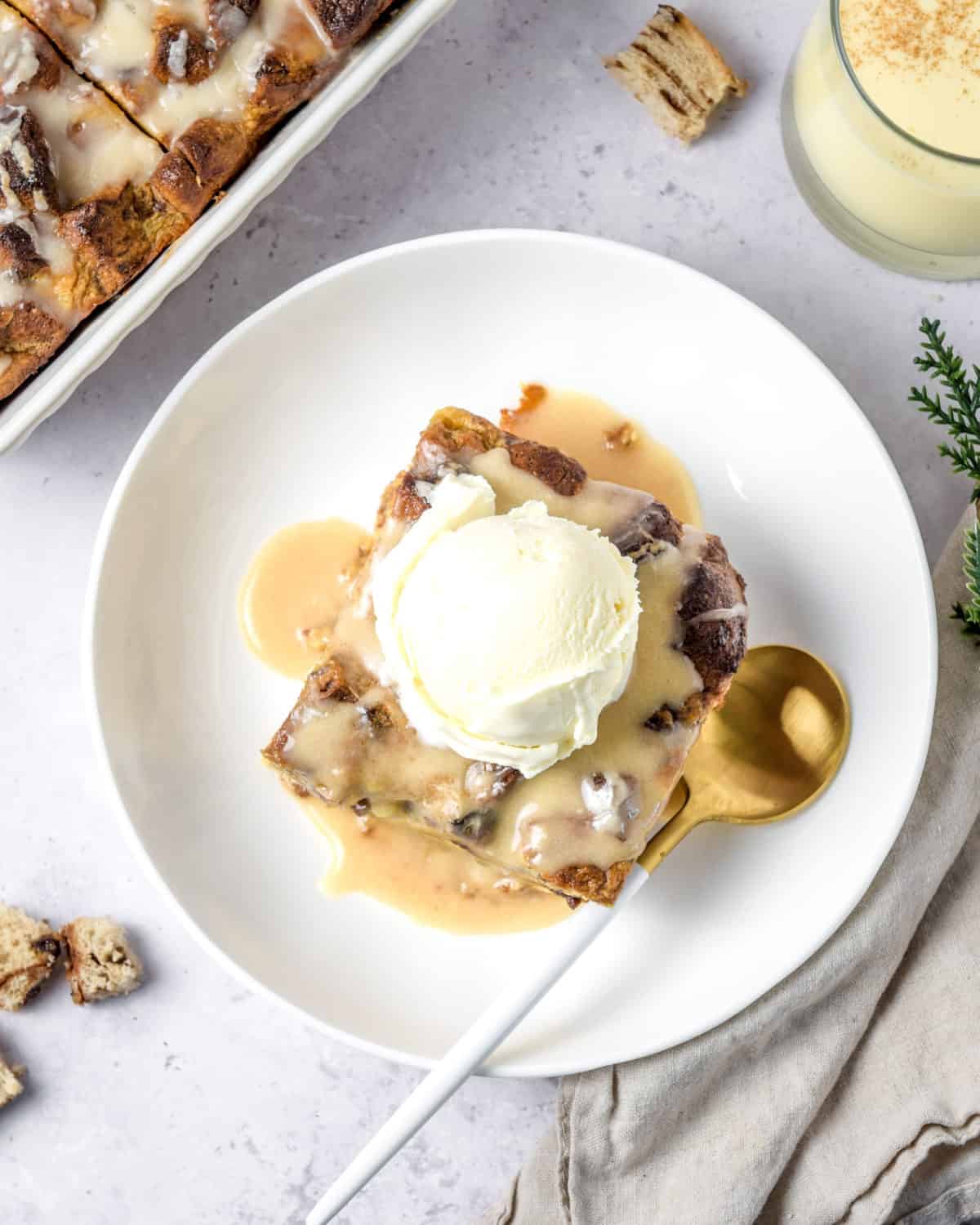An overhead shot of eggnog bread pudding on a white plate with a spoon.