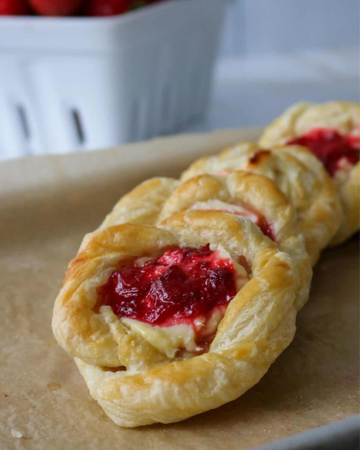 A row of strawberry Danishes on a tray lined with parchment paper.