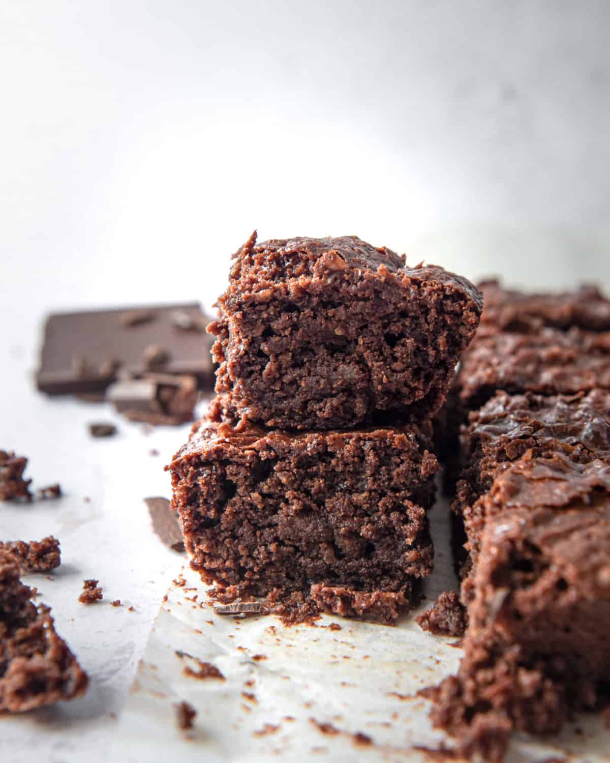 Gooey brownies on parchment paper with lots of crumbs.