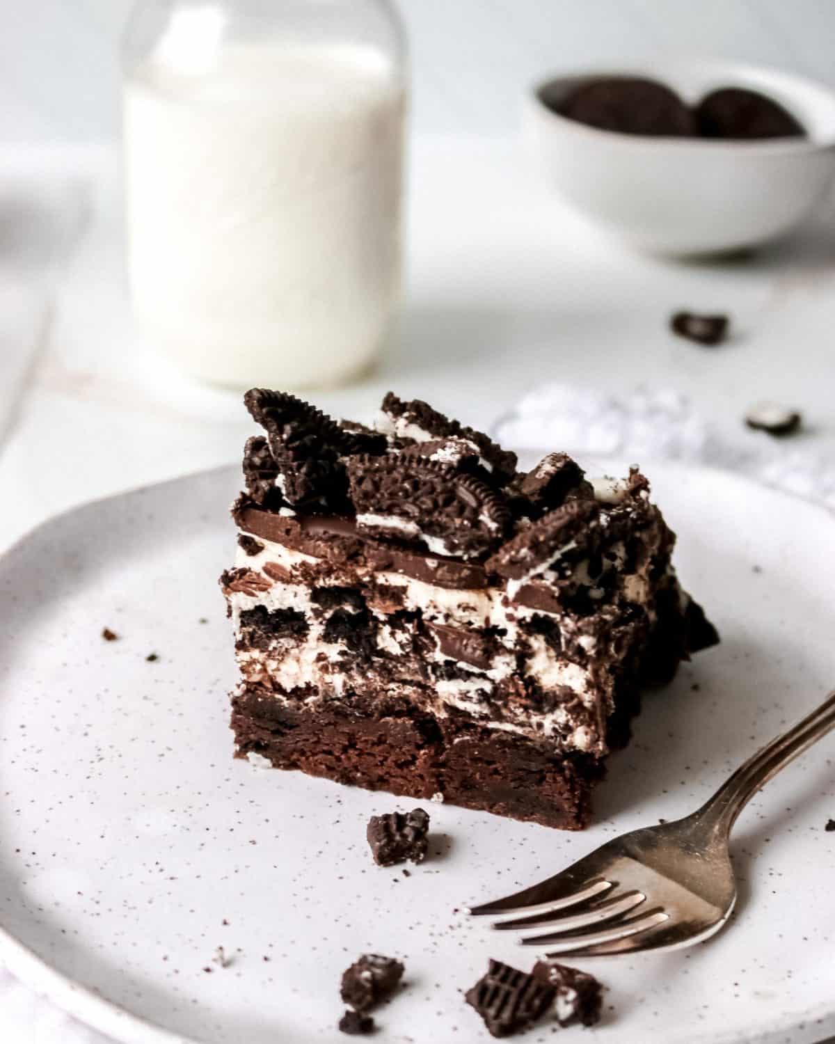 An Oreo brownie on a white plate with a fork and milk.