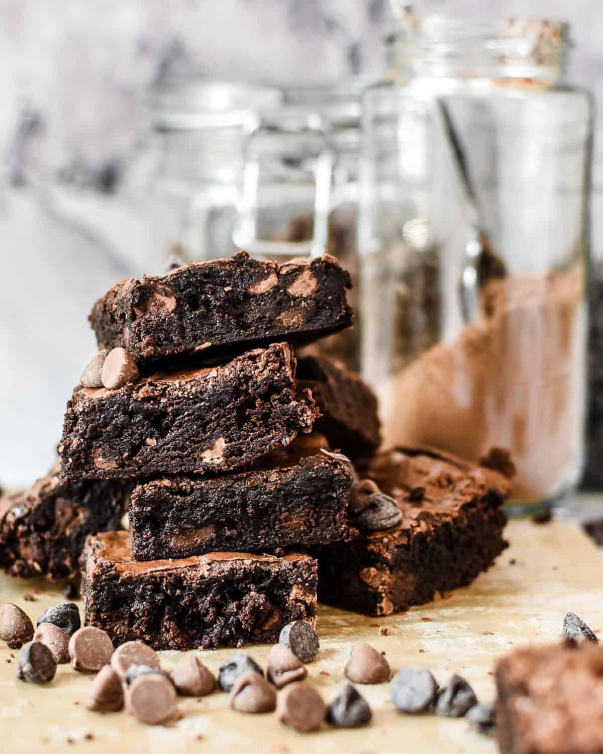 A stack of brownies on top of each other with several chocolate chips scattered on the table around them.