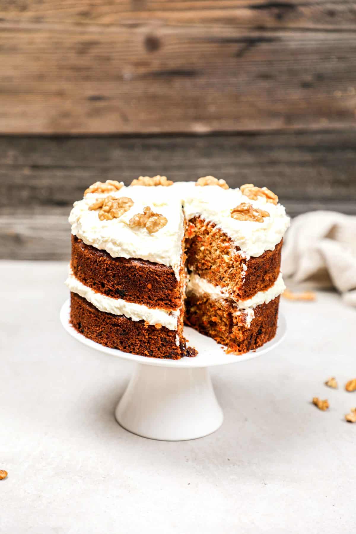 A carrot cake on a cake stand with a slice cut out of it.