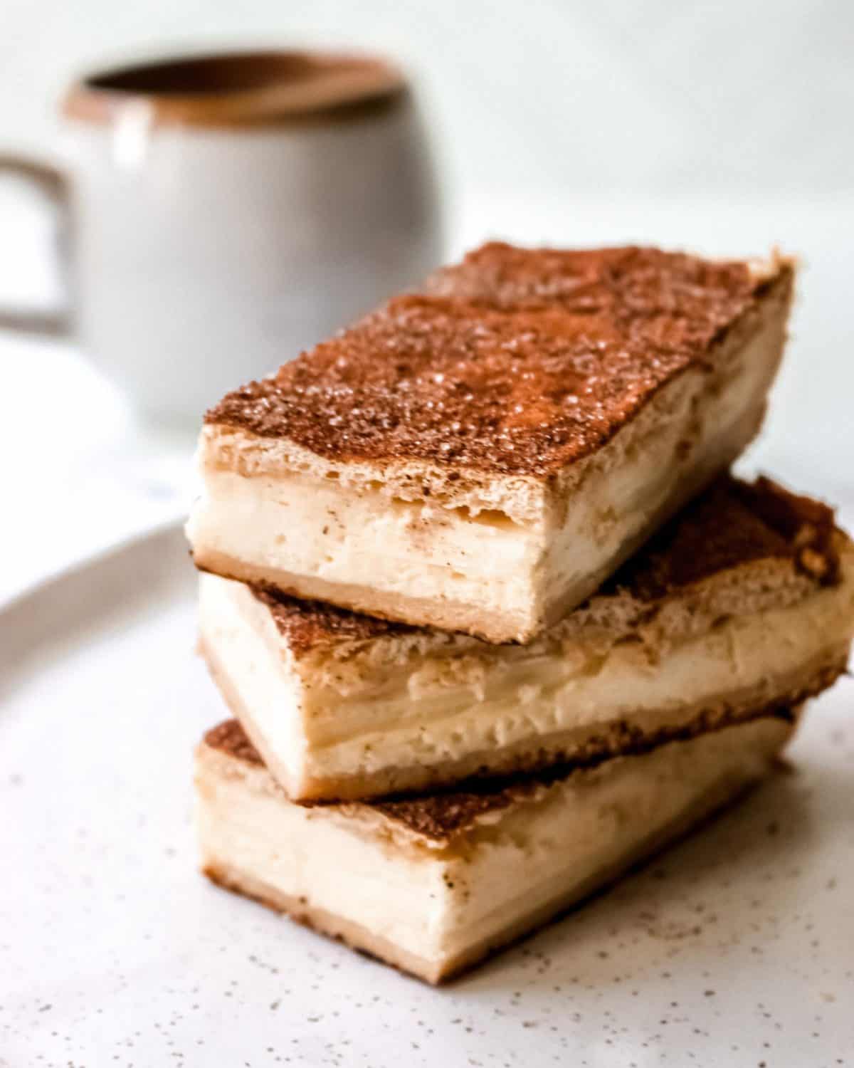 Finished cheesecake bars on a white plate with a cup of coffee in the background.