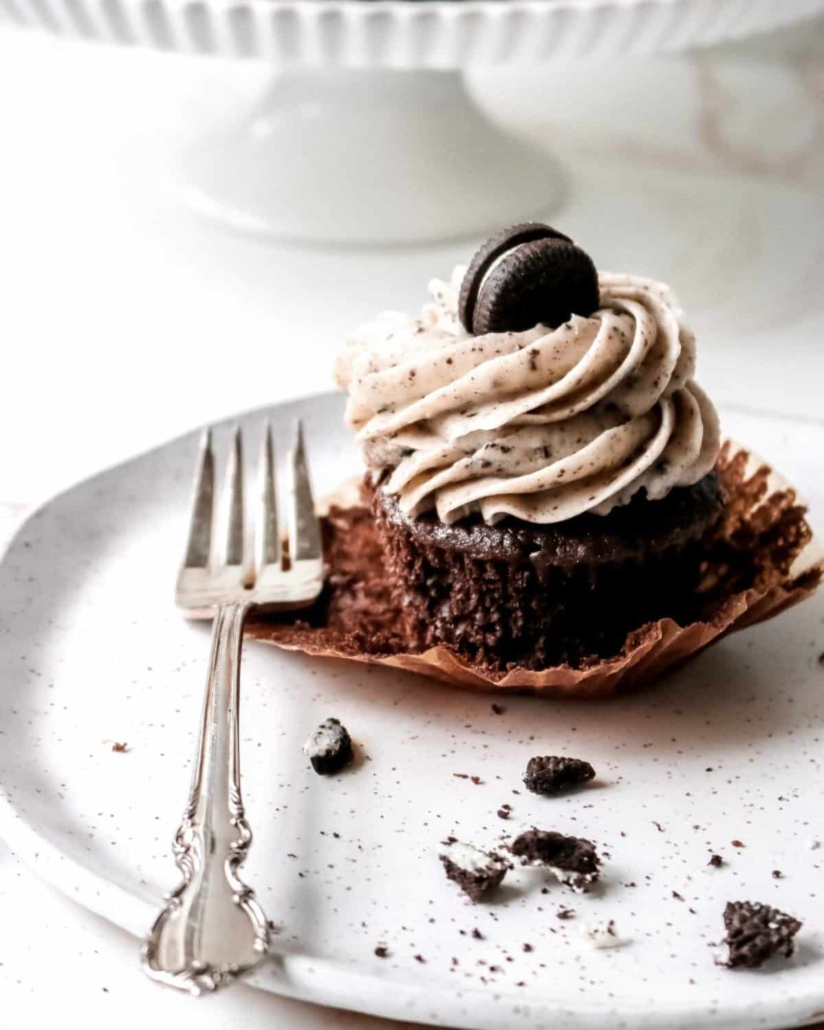 A chocolate cupcake on a plate with a fork and Oreo cookie crumbs.