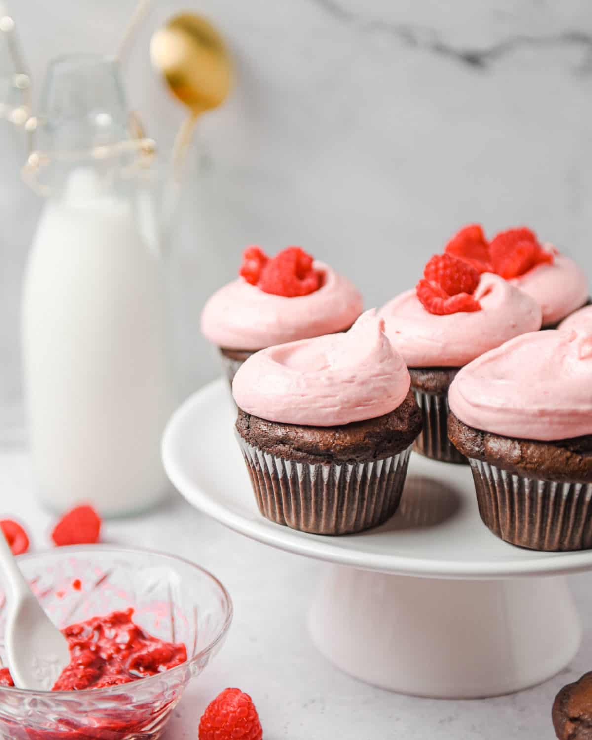 Several chocolate cupcakes with raspberry frosting on a cake stand.