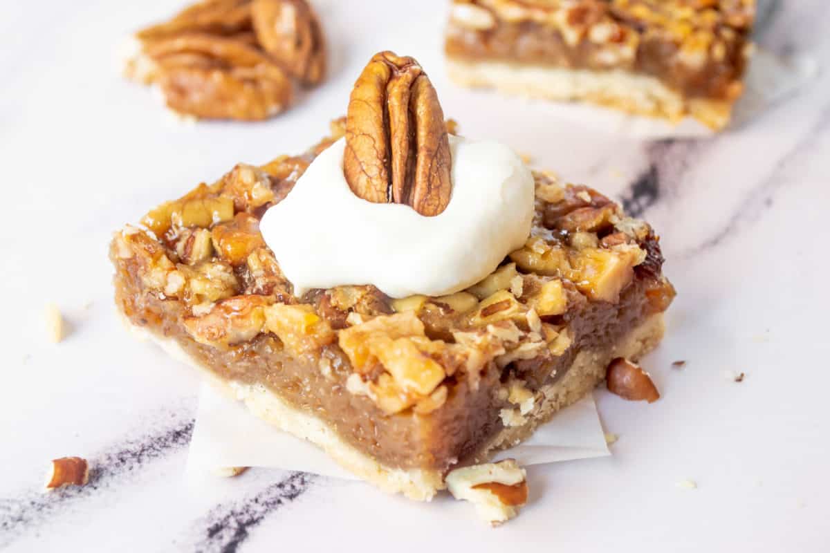 A pecan pie bar up close topped with whipped cream.
