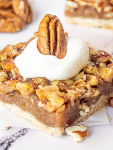A pecan pie bar up close topped with whipped cream.