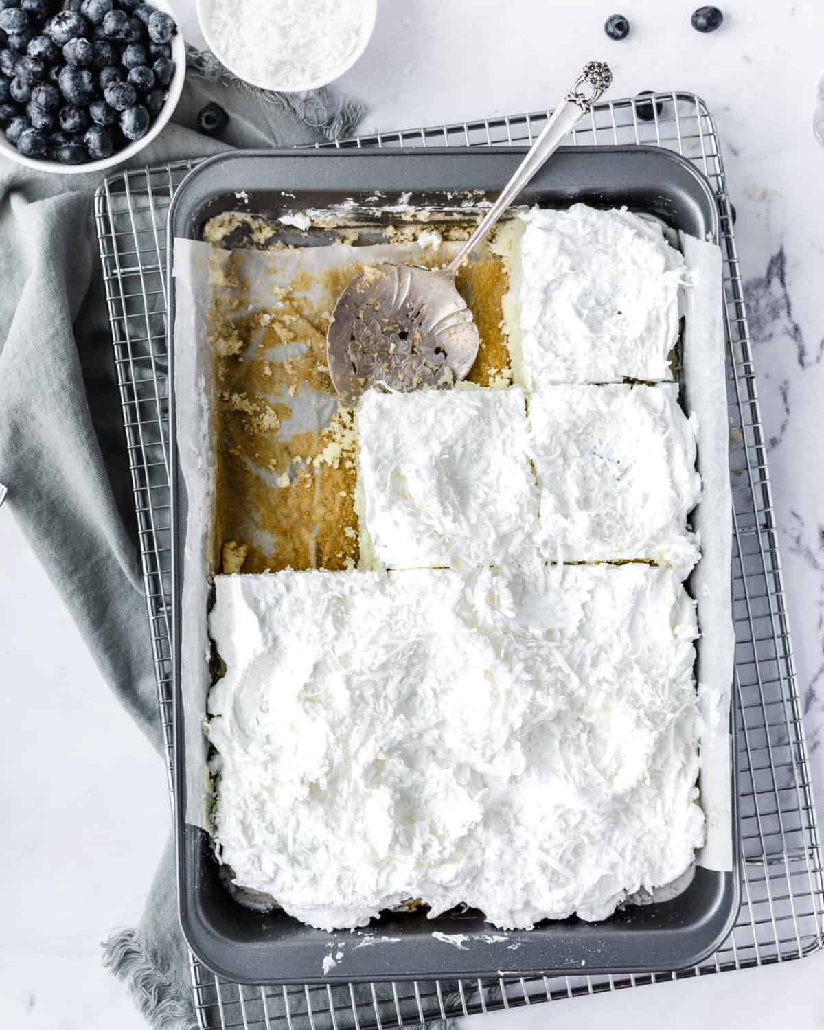 Several pieces of coconut poke cake in a baking pan.