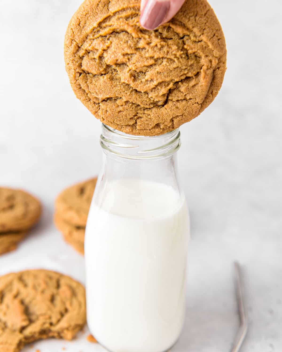A person's hand dunking a cookie in milk.