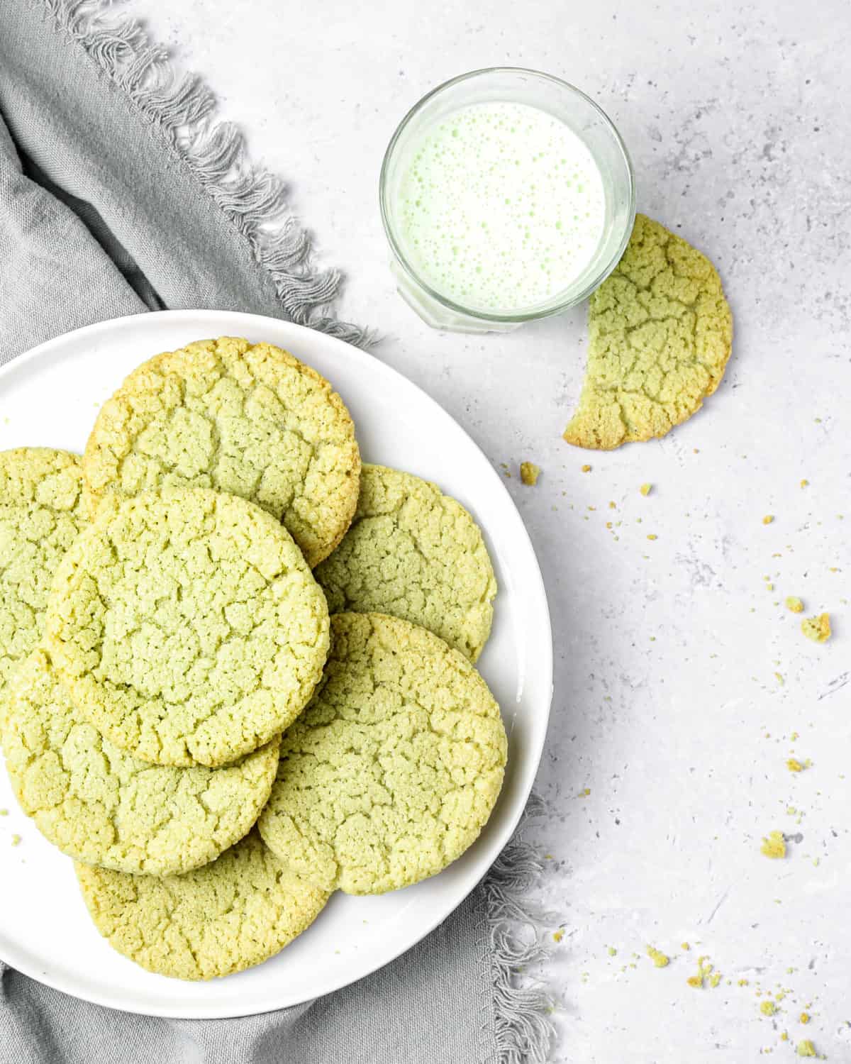 Green cookies on a white plate with a glass of milk.