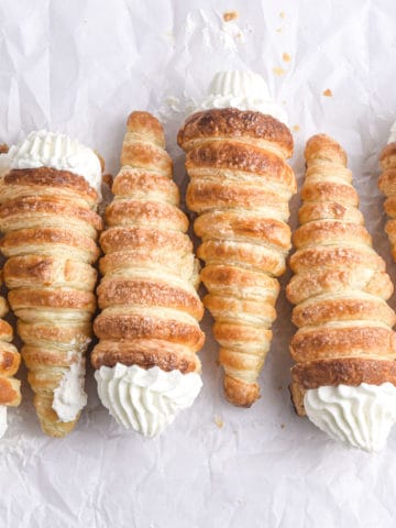 Several cream horns laying on parchment paper.