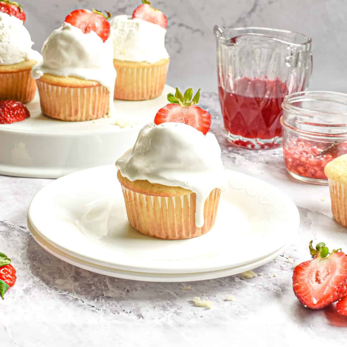 A cupcake on a plate topped with a fresh strawberry halve.