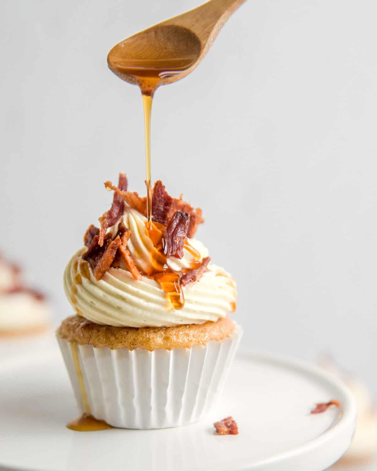 Dripping maple syrup onto the top of a cupcake with a wooden spoon.