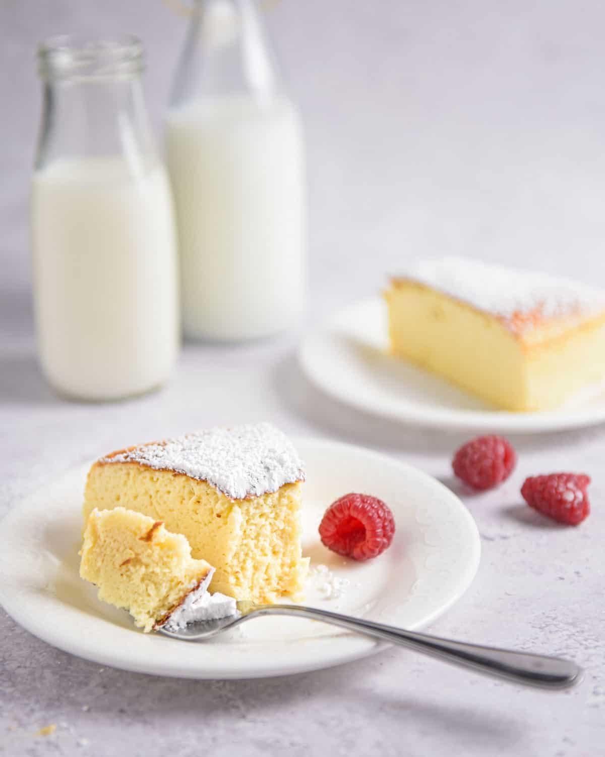 A slice of cheesecake on a plate with milk in the background.