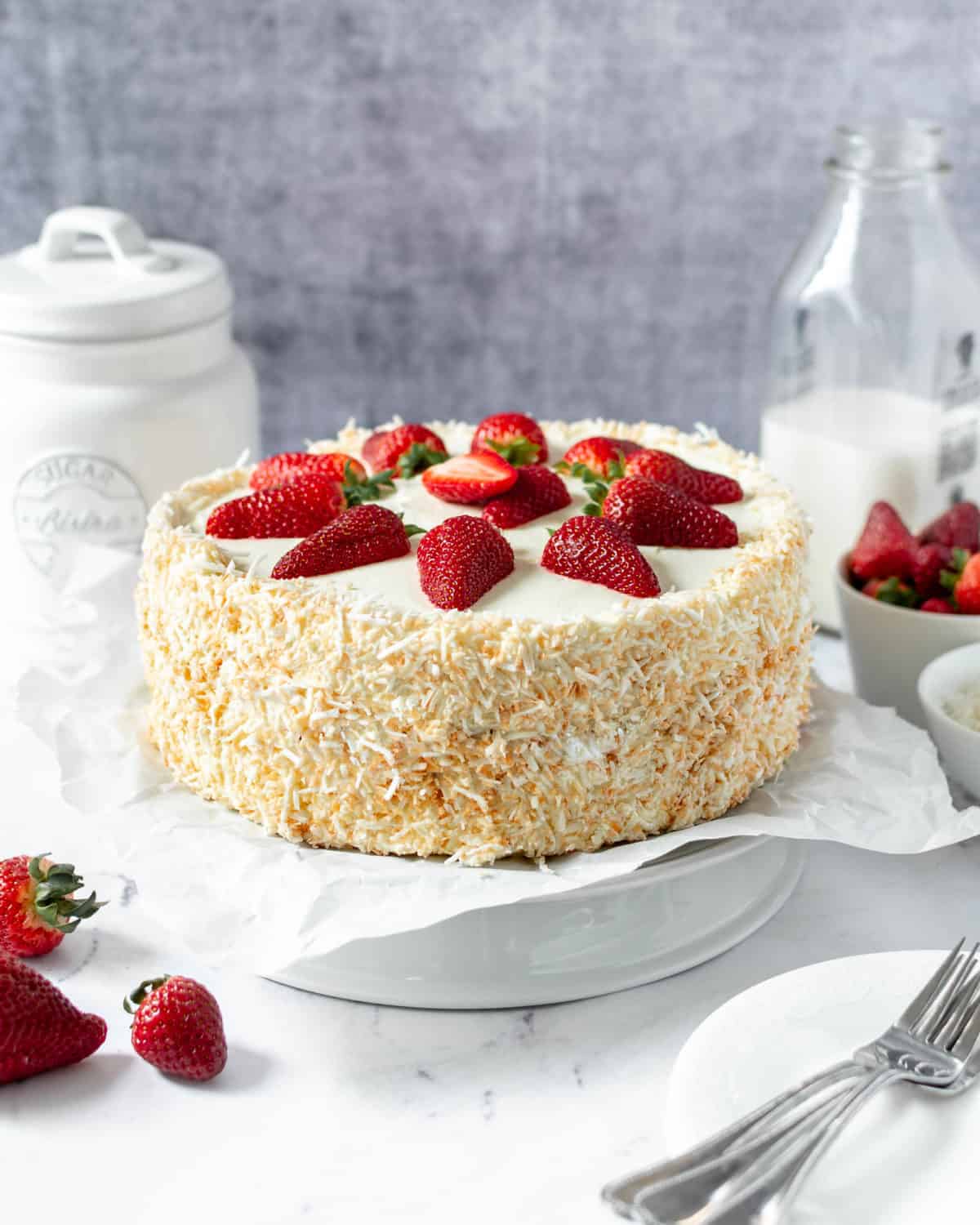 A completed coconut strawberry cake on a cake stand.