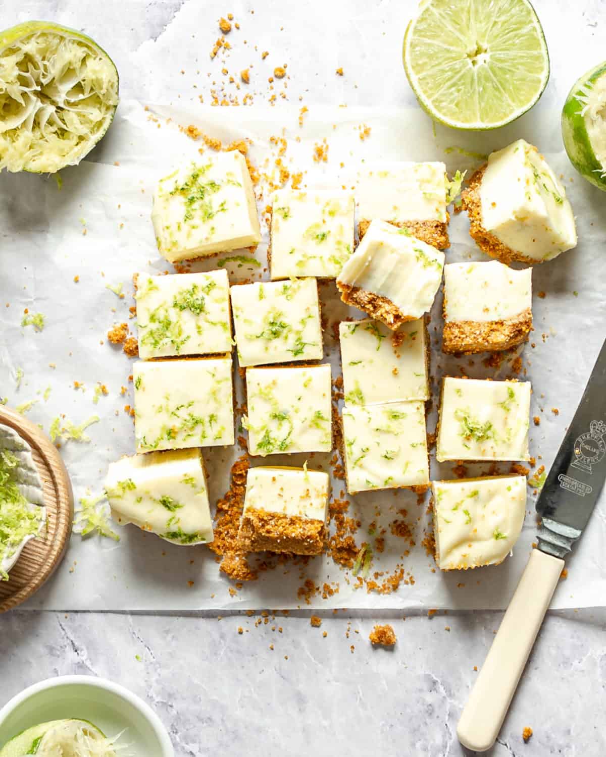 Key lime fudge squares on a table with limes and a knife.