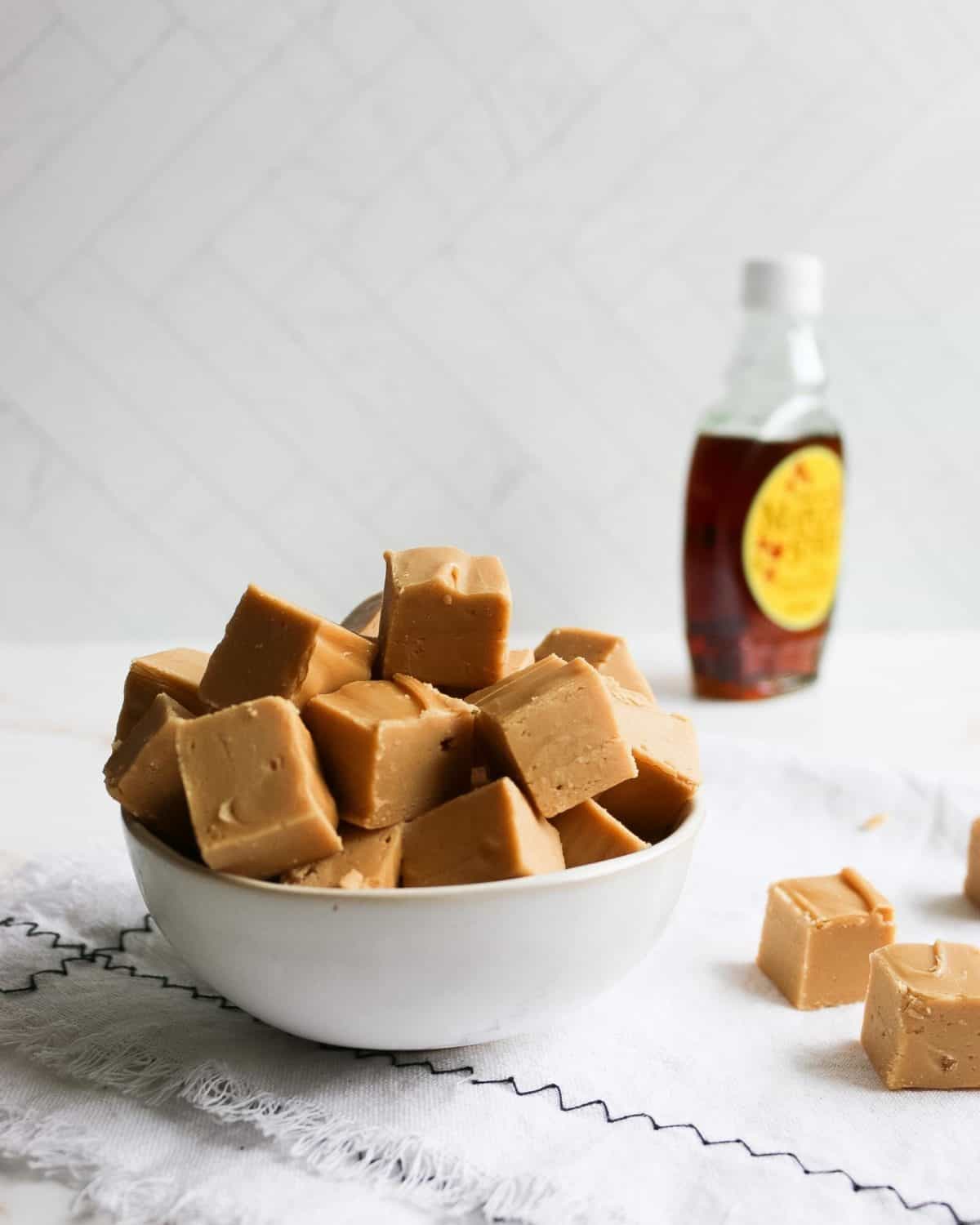 A large bowl of fudge with a bottle of maple syrup in the background.