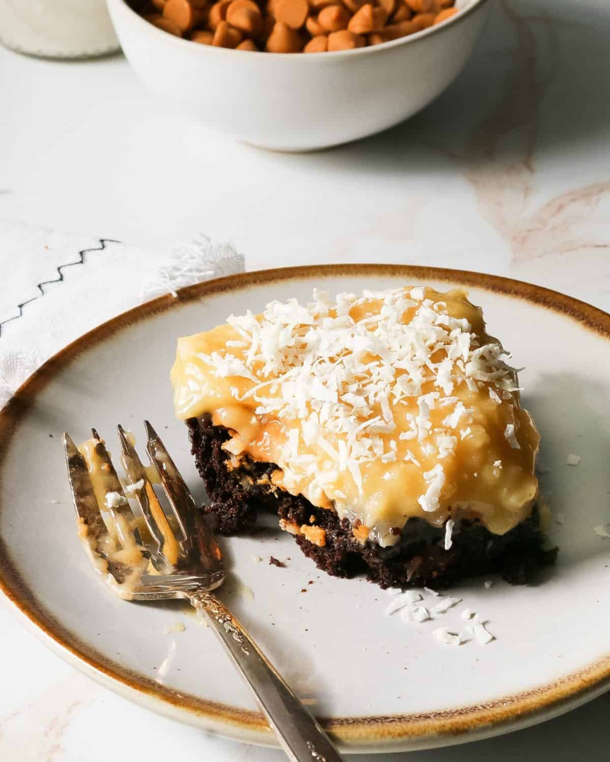 A bite of German chocolate brownie on a plate with a fork and crumbs.