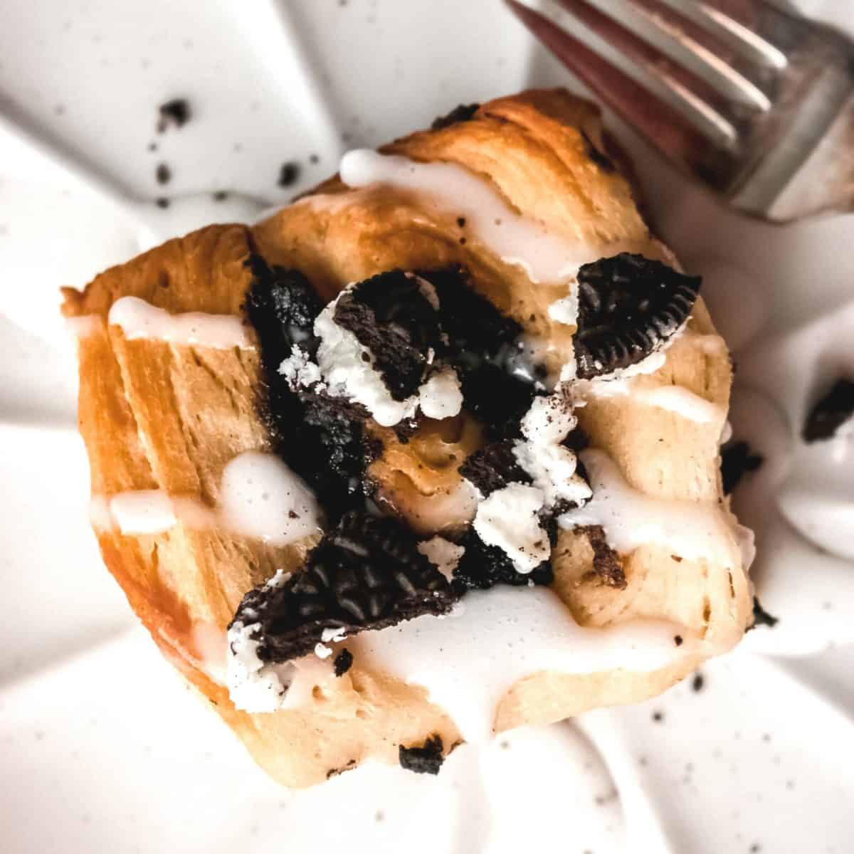 An overhead shot of crushed Oreos and glaze on top of a cinnamon roll.