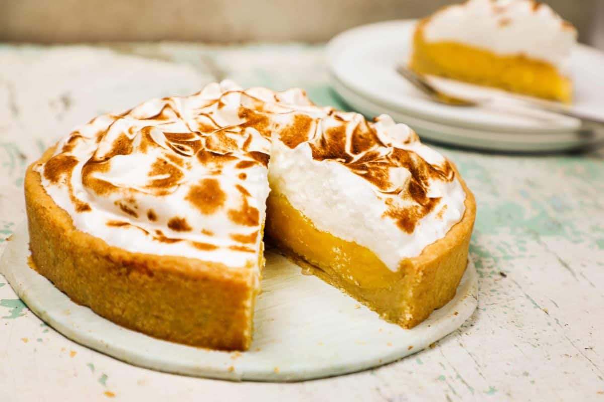 A lemon meringue pie on a table with a slice cut out of it.