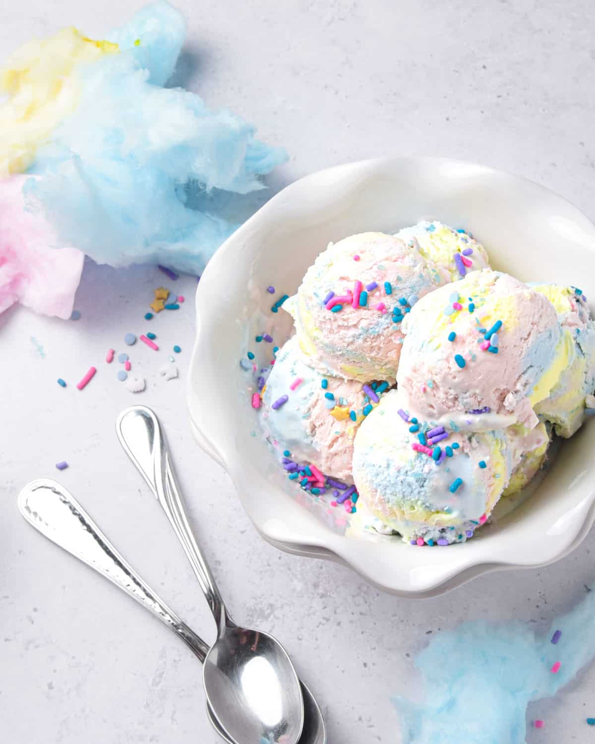 Scoops of yellow, pink, and blue colored ice cream in a bowl with two spoons.