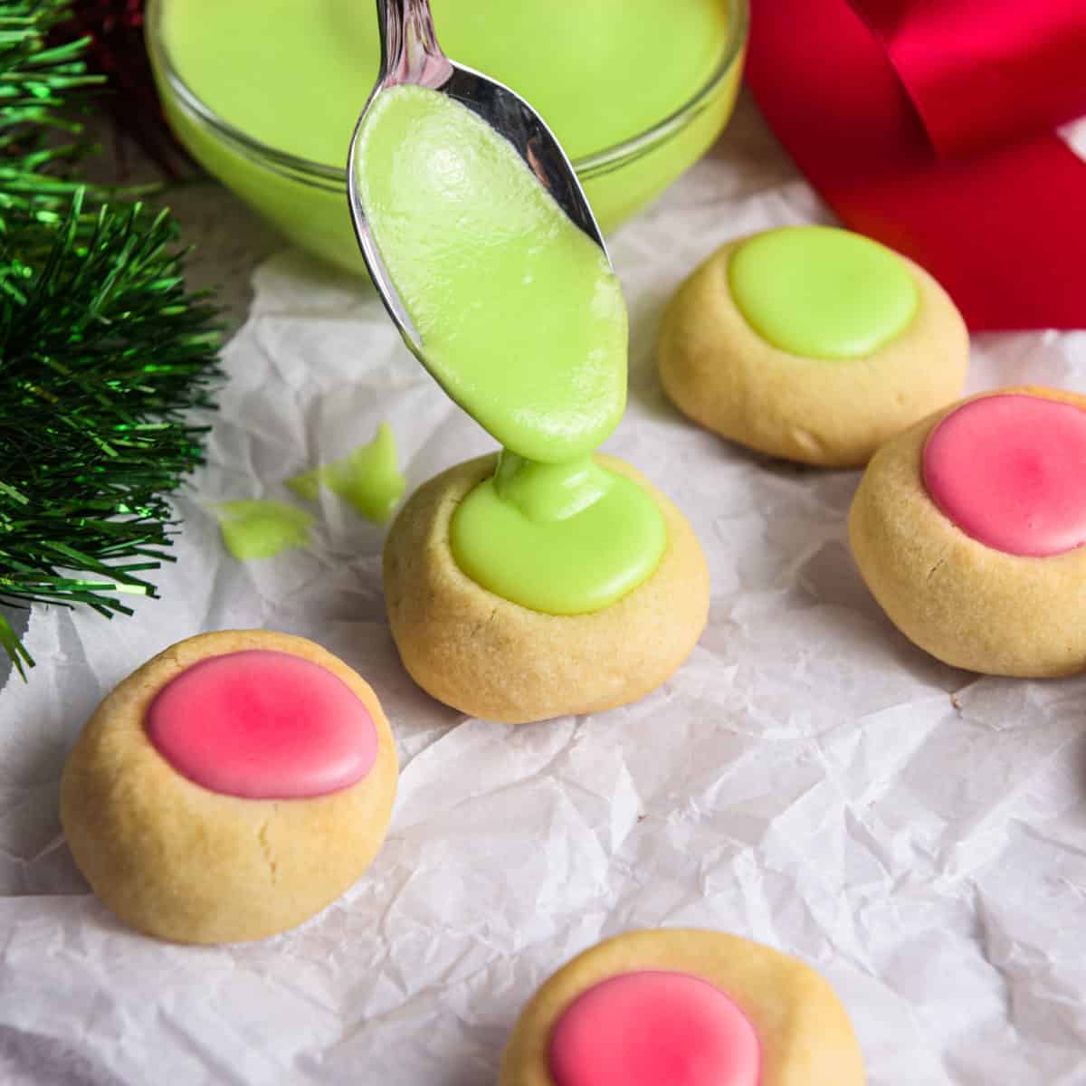 Adding red and green icing on top of thumbprint cookies.