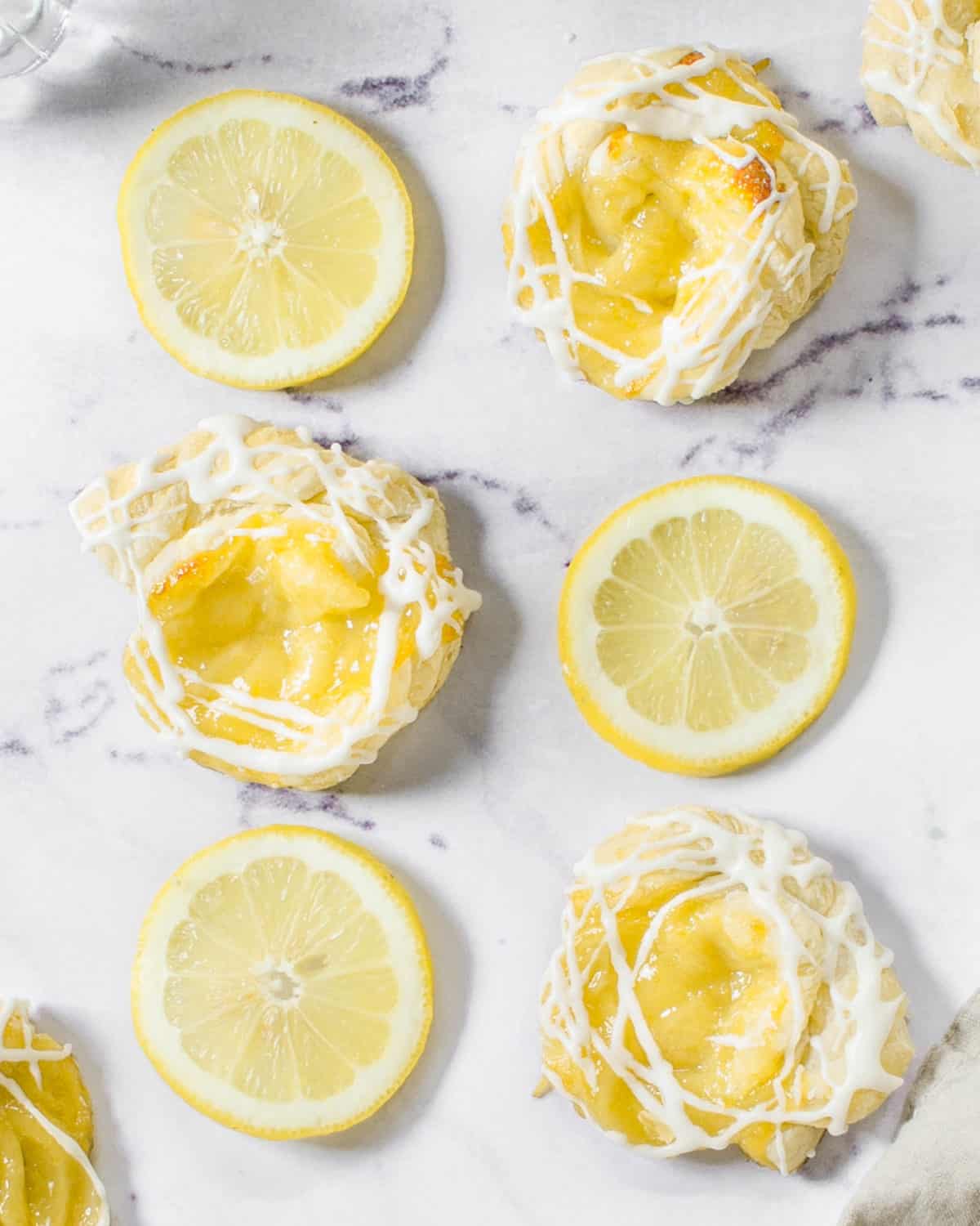 Lemon curd puff pastries spread out on a table with lemons.