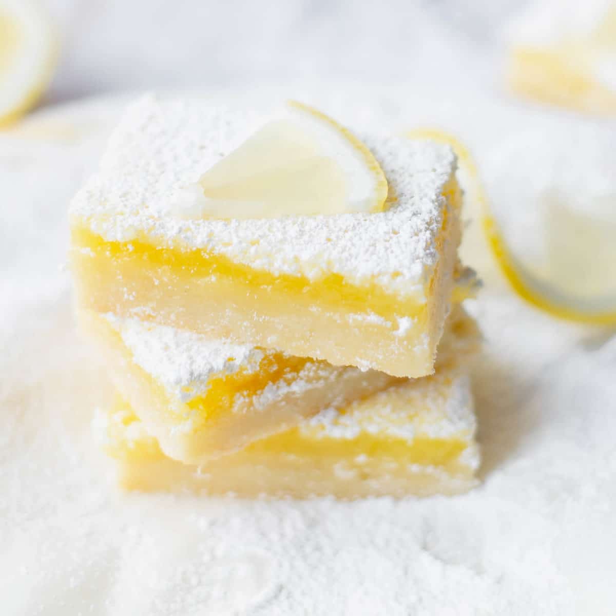 Three lemon bars with powdered sugar topped with a lemon slice.