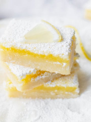 Three lemon bars with powdered sugar topped with a lemon slice.