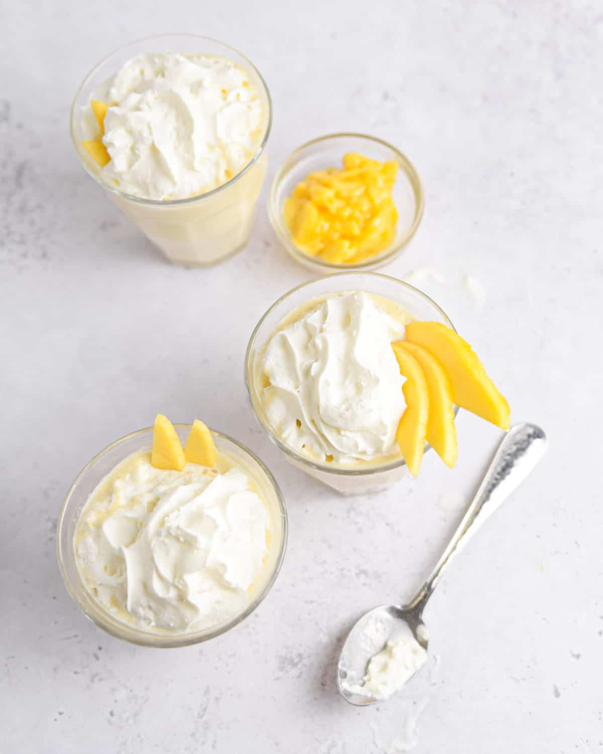 Several mango milkshakes topped with whipped cream and fresh mango.